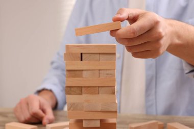 Jenga oynuyorum. Masada tahta bloklar olan kule inşa eden adam, yakın plan.