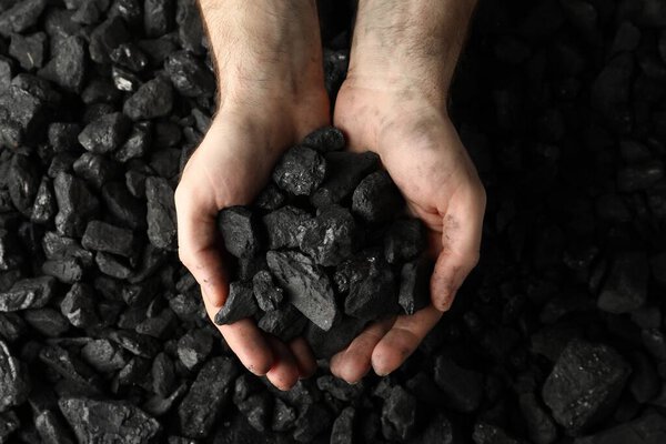 Человек держит уголь в руках над кучей, вид сверху