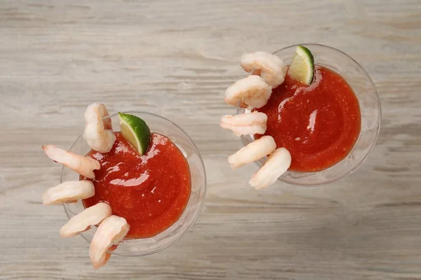 Tasty shrimp cocktail with sauce and lime in glasses on wooden table, flat lay