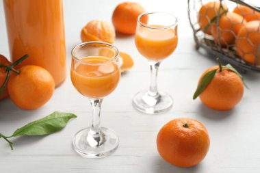 Lezzetli mandalina likörü ve beyaz ahşap masada taze meyveler.