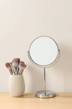 Odadaki ahşap tuvalet masasında ayna ve makyaj fırçaları.