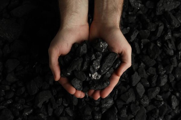 Человек держит уголь в руках над кучей, вид сверху