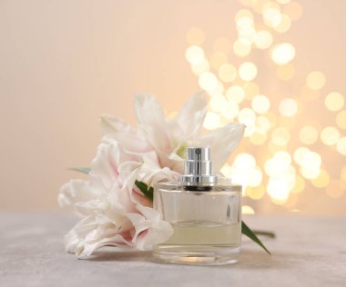Bir şişe parfüm ve güzel zambak çiçekleri bulanık ışıklarla bej arka planda.