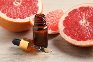 Bir şişe greyfurt yağı ve hafif ahşap masada taze meyveler.