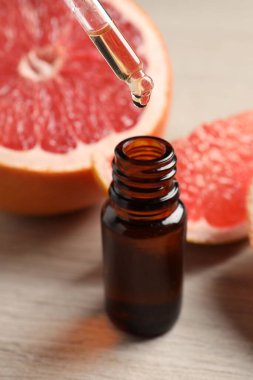 Pipetten şişeye akan greyfurt yağı ve açık ahşap masada taze meyveler.