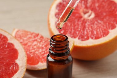 Pipetten şişeye damlayan greyfurt yağı ve arka planda taze meyveler, yakın plan