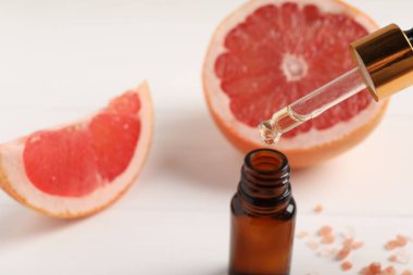 Pipetten şişeye greyfurt yağı damlıyor ve beyaz masaya taze meyve dökülüyor. Yakın plan. Metin için boşluk