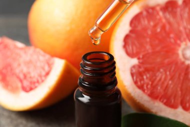 Pipetten şişeye greyfurt yağı damlıyor ve masada taze meyveler, yakın plan.