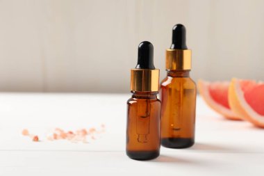 Beyaz ahşap masadaki şişelerde greyfurt yağı, yakın plan. Metin için boşluk