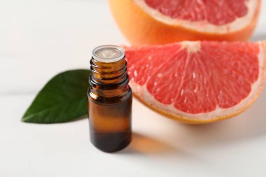 Şişede greyfurt yağı, beyaz masada yaprak ve meyve, yakın plan.