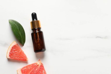 Şişede greyfurt yağı, beyaz mermer masa üzerinde yaprak ve meyve kesimi, düz zemin. Metin için boşluk