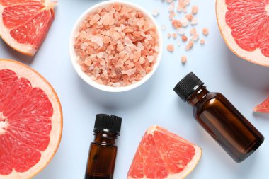 Şişelerde greyfurt yağı, deniz tuzu ve açık mavi masada meyve kesimi.