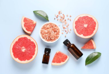 Şişelerde greyfurt yağı, deniz tuzu ve açık mavi masada meyve kesimi.