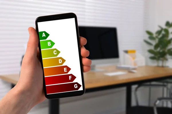 Energy efficiency. Man using smartphone with colorful rating on display indoors, closeup