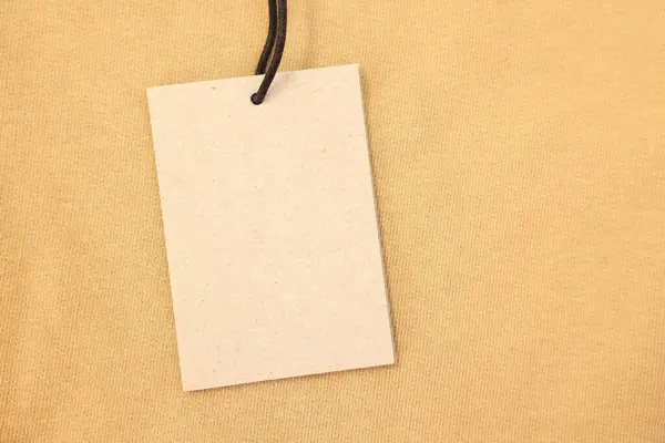 Cardboard tag on beige garment, top view. Space for text