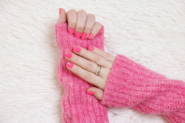 Woman showing her manicured hands with pink nail polish on faux fur mat, top view