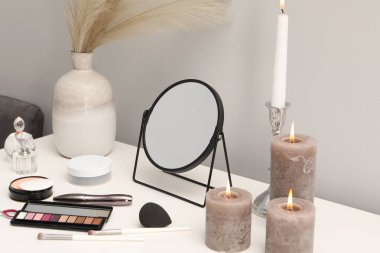 Aynalı giyinme masası, kozmetik ürünler, parfümler ve makyaj odasında yanan mumlar.