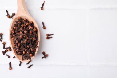 Beyaz fayanslı masa üzerinde aromatik kurutulmuş karanfil tomurcukları olan kaşık, üst manzara. Metin için boşluk