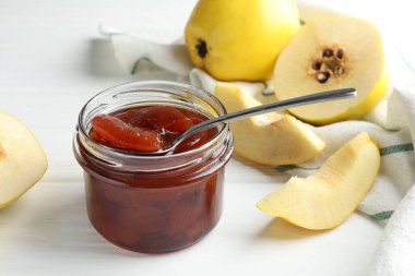 Kavanozda ev yapımı ayva reçeli, beyaz ahşap masada kaşık ve meyveler, yakın plan.