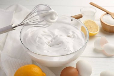 Krem şantili kase, çırpma ve malzemeler beyaz ahşap masada.