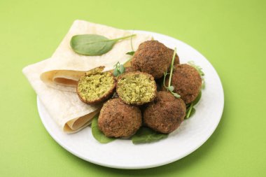 Yeşil arka planda nefis falafel topları, bitkiler ve lavaş.