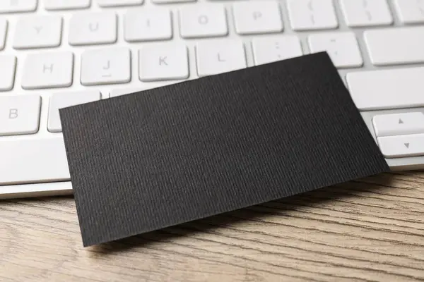 Blank black business card and computer keyboard on wooden table, closeup. Mockup for design