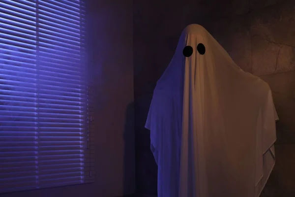 Creepy ghost. Woman covered with sheet near window in color lights, space for text