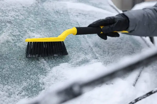 Man cleaning snow from car windshield outdoors, closeup
