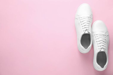 Pembe arka planda bir çift şık beyaz spor ayakkabı, üst manzara. Metin için boşluk