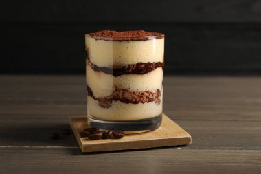 Bardakta nefis tiramisu ve ahşap masada kahve çekirdekleri, yakın plan.