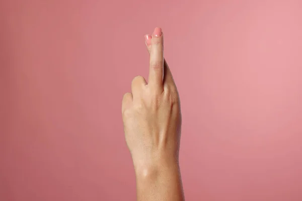 Woman crossing her fingers on pink background, closeup
