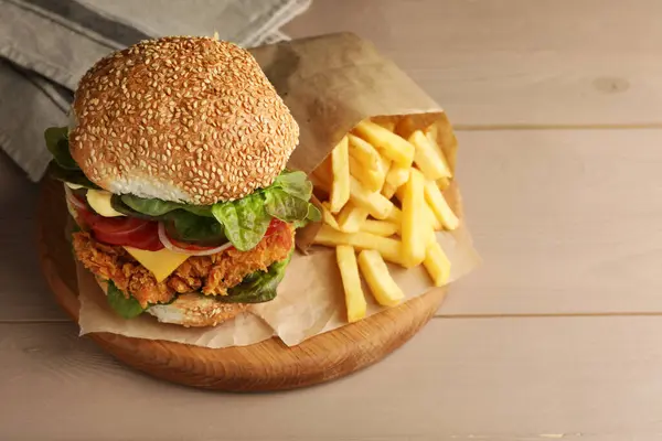 Delicious burger with crispy chicken patty and french fries on wooden table