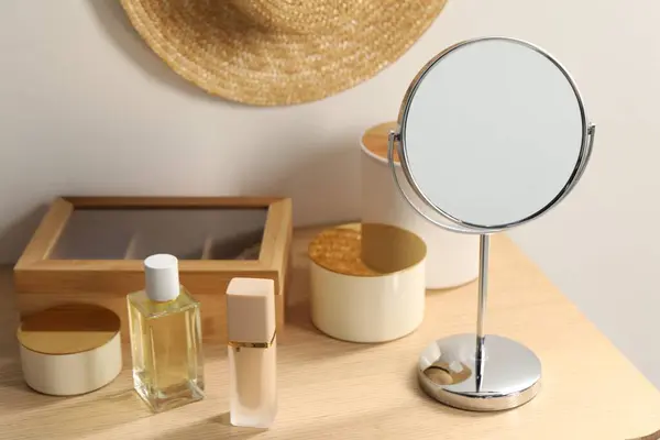 Mirror, perfume and makeup products on dressing table in room