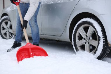 Adam arabanın yanında kürekle karları kaldırıyor, yakın plan.