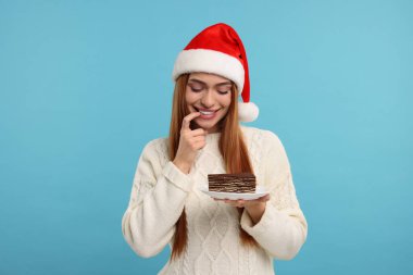 Noel Baba şapkalı genç bir kadın açık mavi arka planda lezzetli bir pastayla