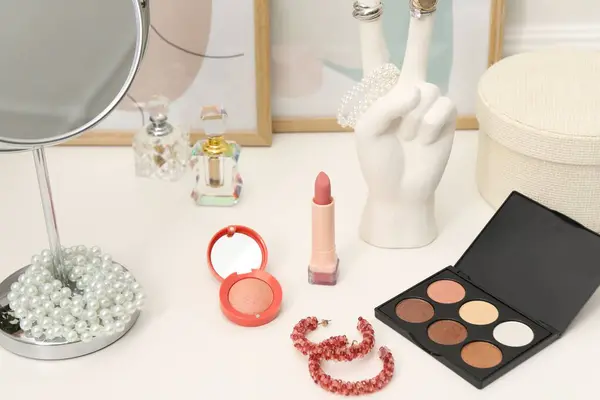 Mirror, cosmetic products, perfumes and jewelry on white dressing table, closeup