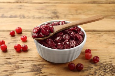 Lezzetli kuru kızılcıklar kasede ve taze olanlar ahşap masada, yakın plan.