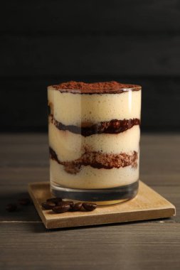 Bardakta nefis tiramisu ve ahşap masada kahve çekirdekleri.