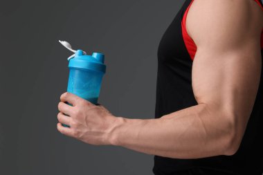 Gri arka planda protein titreten kaslı genç adam, yakın plan.