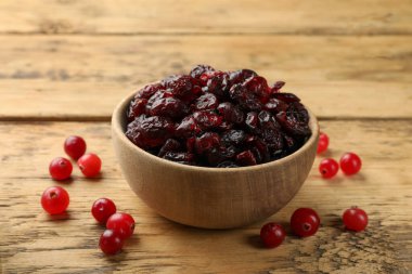 Lezzetli kuru kızılcıklar kasede ve taze olanlar ahşap masada, yakın plan.