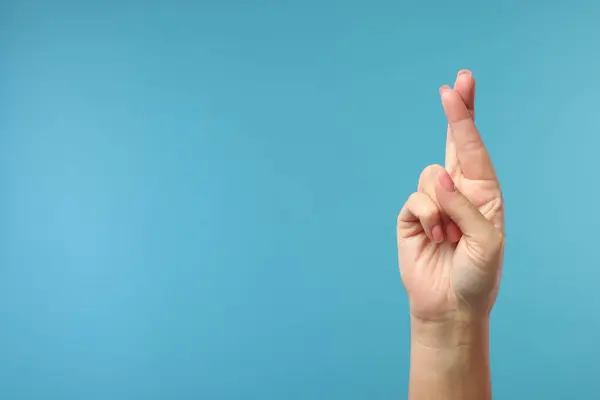 Woman crossing her fingers on light blue background, closeup. Space for text