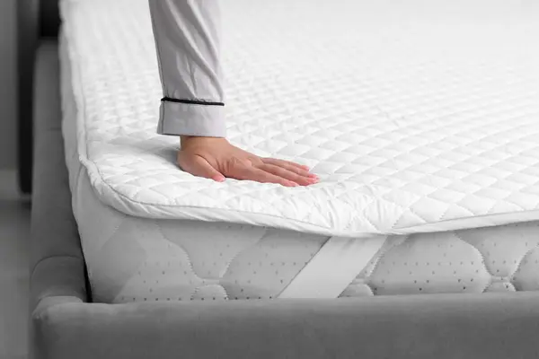 Woman touching new soft mattress on grey bed indoors. closeup