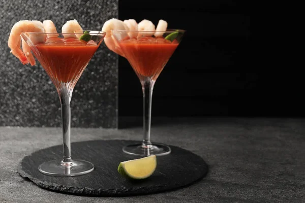 Tasty shrimp cocktail with sauce in glasses and lime on grey table, space for text