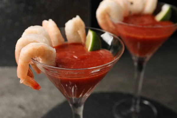 Tasty shrimp cocktail with sauce and lime in glasses on grey table, closeup