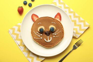 Çocuklar için yaratıcı hizmet. Sarı arka planda krep, böğürtlen, krema, muz ve çikolata ezmesinden yapılmış şirin bir kedi tabağı.