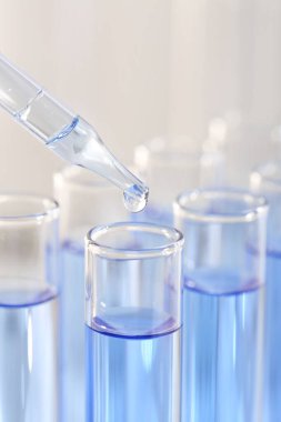 Laboratuvar analizi. Pipetten açık mavi sıvıyı bulanık arkaplanda cam test tüpüne damlatarak, yakın plan