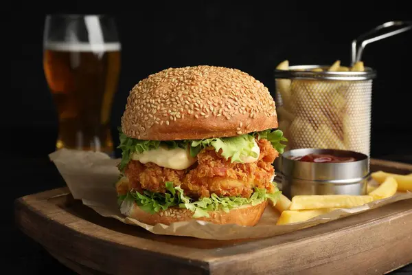 Delicious burger with crispy chicken patty, french fries and sauce on table
