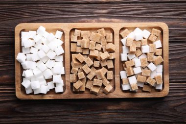 Tahta masanın üzerinde kahverengi ve beyaz şeker küpleri olan tepsi, üst manzara.