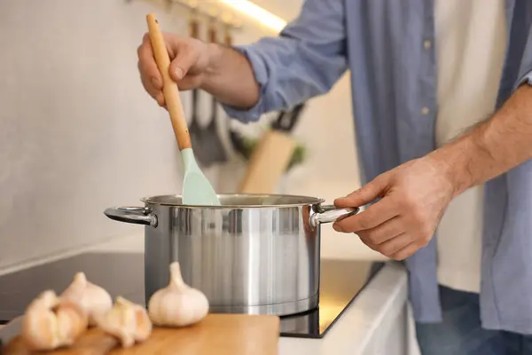 Man cooking delicious soup in kitchen, closeup
