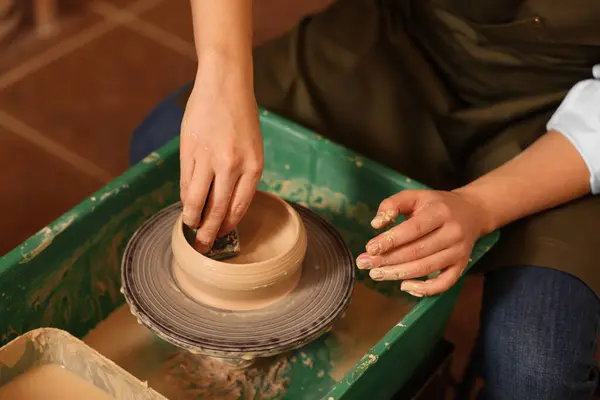 Clay crafting. Woman making bowl on potter\'s wheel indoors, closeup
